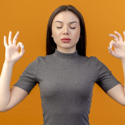 peaceful young pretty woman meditating with closed eyes isolated on orange background